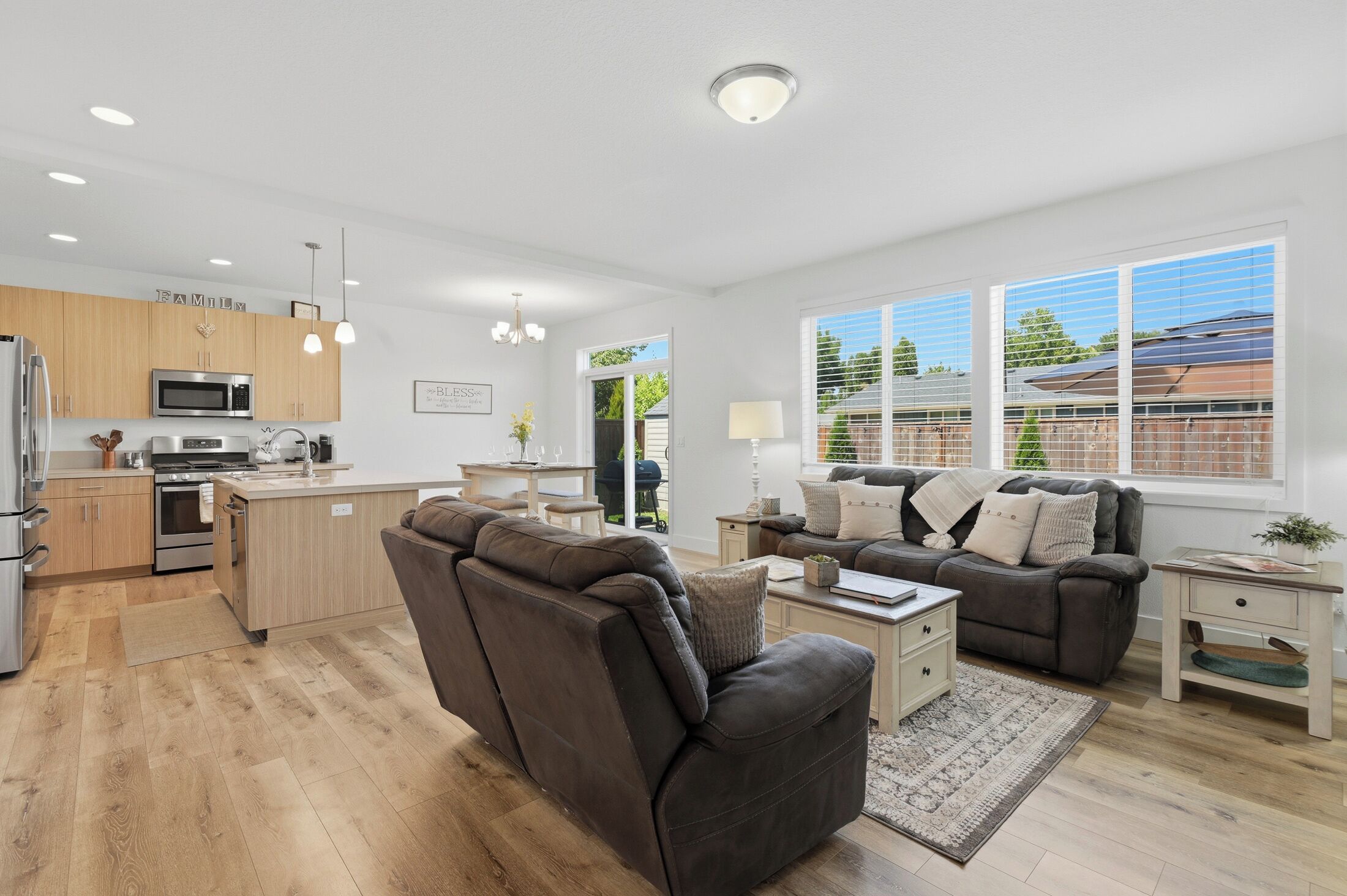 A modern kitchen with built-in appliances, a dining area with a sofa and table, and large windows offering a view of the outdoors.