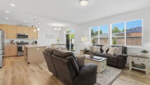 A modern kitchen with built-in appliances, a dining area with a sofa and table, and large windows offering a view of the outdoors. - Page Place: Modern Extended Stay in Newberg, Dog-Friendly (Newberg)
