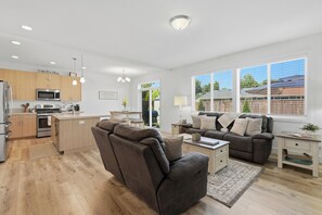 Eine moderne Küche mit Einbaugeräten, eine Essecke mit Sofa und Tisch sowie große Fenster mit Blick ins Freie.
