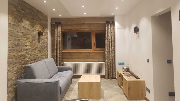 A modern living room with a grey sofa, wooden coffee table, and a stone wall. - Luxury 3-star Apartment Rental for 6 People (Tignes)
