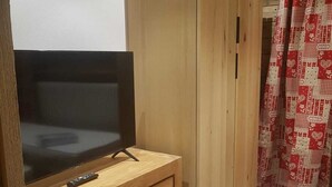 A room with a television on a wooden cabinet, a wardrobe, and a patterned curtain. - Luxury 3-star Apartment Rental for 6 People (Tignes)