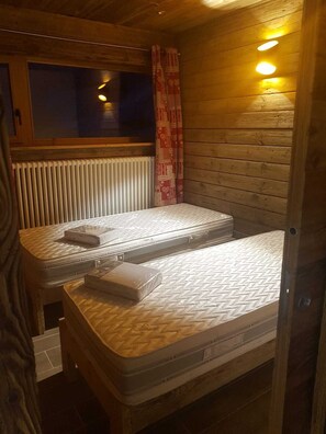 A compact room with two beds, a window, and a radiator. - Luxury 3-star Apartment Rental for 6 People (Tignes)