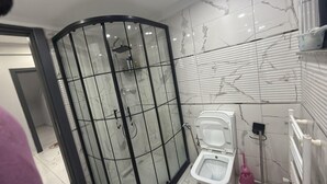 A modern bathroom with a glass-enclosed shower, a toilet, and a white tiled wall with a marble-like pattern. - Cozy 2 Seprate Bedroom Apartment in Küçükçekmece With Stunning Views (Istanbul)