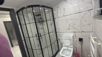 A modern bathroom with a glass-enclosed shower, a toilet, and a white tiled wall with a marble-like pattern.