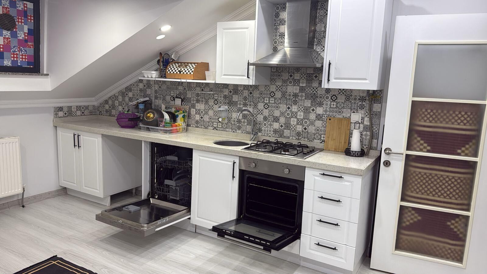 Una cocina con armarios blancos, horno empotrado, cocina a gas y salpicadero decorado.
