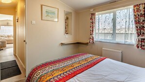 Un dormitorio con cama, ventana con cortinas, radiador y puerta que da a otra habitación.