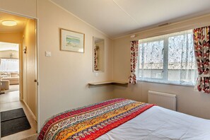 Ein Schlafzimmer mit Bett, einem Vorhangfenster, einer Heizung und einer Tür zu einem anderen Raum.