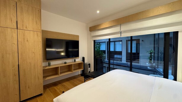 A modern bedroom with a large bed, a TV mounted on a wooden cabinet, and a balcony with a view. - w Enchanting Loft in the Heart of Roma Sur (Mexico City)