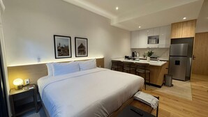 A hotel room with a bed, bedside table, lamp, and a kitchenette with a refrigerator, stove, and bar stools. - w Enchanting Loft in the Heart of Roma Sur (Mexico City)