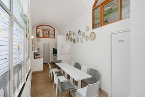 Un espace repas avec une longue table et des chaises, une cuisine en arrière-plan et des assiettes décoratives accrochées au mur.
