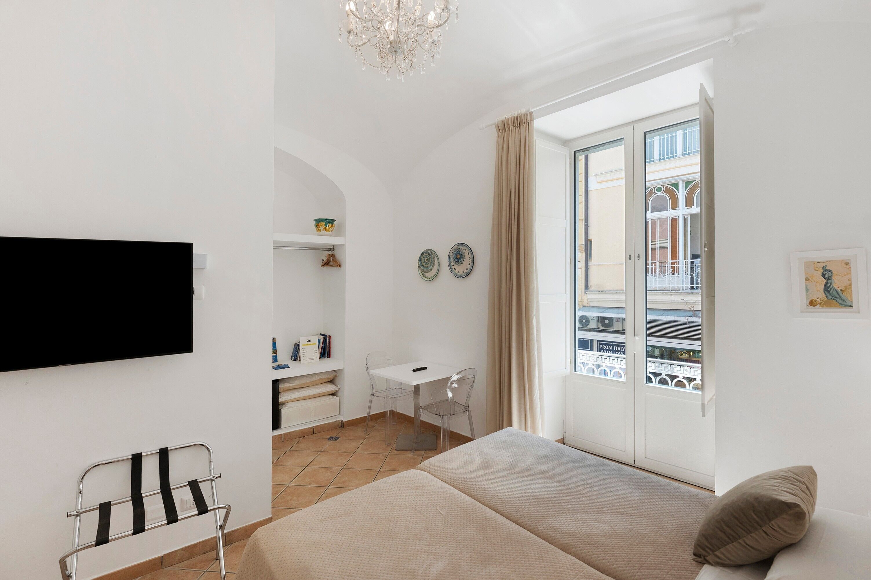 Hotelkamer met een bed, bureau, stoel, televisie, raam met uitzicht en een kroonluchter.