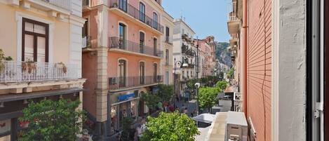 A narrow street with multi-story buildings, balconies, and a shop with a visible sign.