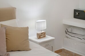 A neatly made bed with a white and beige pillow, a bedside table with a lamp, and a small drawer.