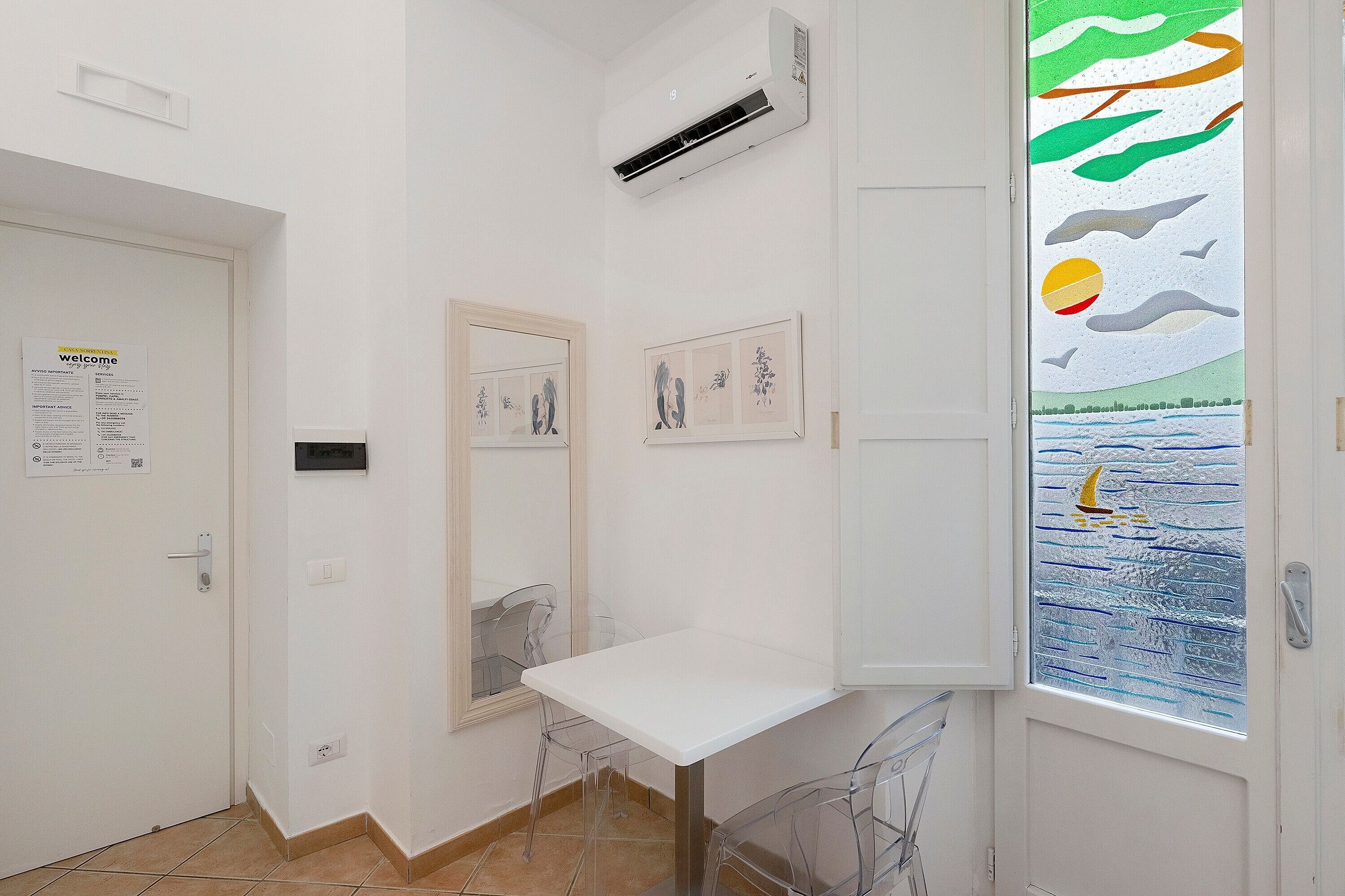 A hallway with a white door, a small table, and a window with a colorful mural.