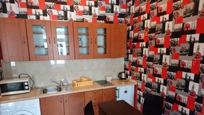 A compact kitchen with wooden cabinets, a washing machine, a microwave, and a small refrigerator. - Charming studio apartment in the heart of Kraków (Kraków)