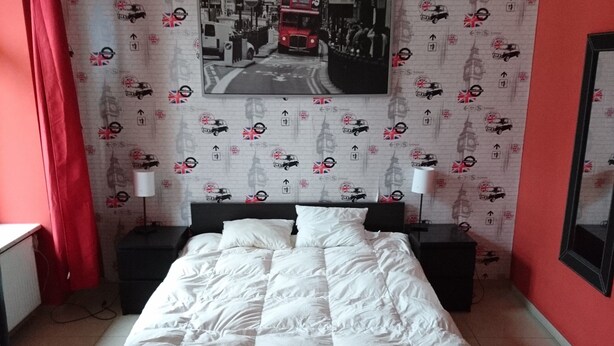 A bedroom with a bed, two bedside tables, a wall-mounted TV, and a red curtain. - Charming studio apartment in the heart of Kraków (Kraków)