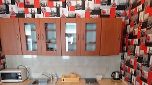 A compact kitchen with wooden cabinets, a microwave, a sink, and a small refrigerator. There is a table with two chairs and a washing machine in the corner. - Charming studio apartment in the heart of Kraków (Kraków)