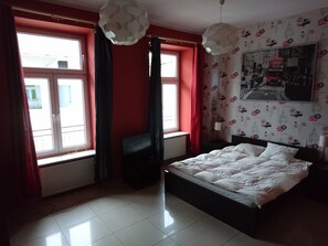 Ein Schlafzimmer mit einem Bett, einem Fenster mit Vorhängen, einem Heizkörper und einer Wand mit strukturiertem Wandpapier.