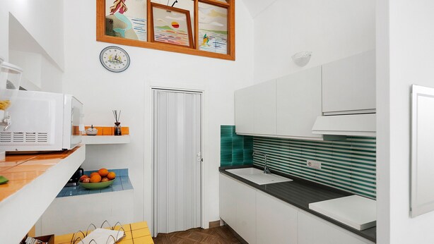 A compact kitchen with a sink, a microwave, and a bowl of fruit on the counter. - Sorrentina Guest House – Quadruple Room with Balcony and Wi-Fi (Sorrento)