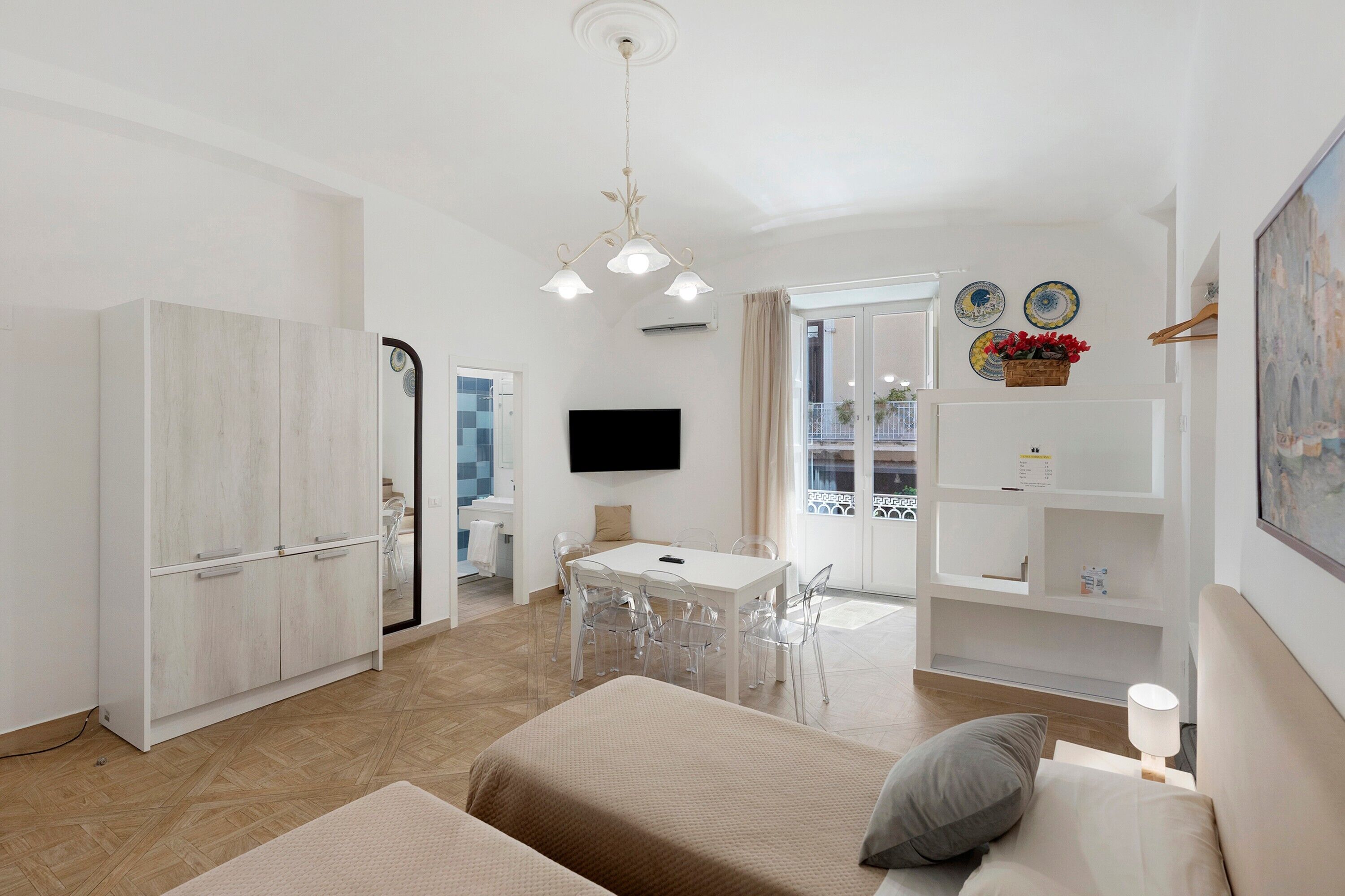 Een moderne, goed verlichte woonkamer met een bank, een eethoek met tafel en stoelen, een keuken met een koelkast, en een tv aan de muur.