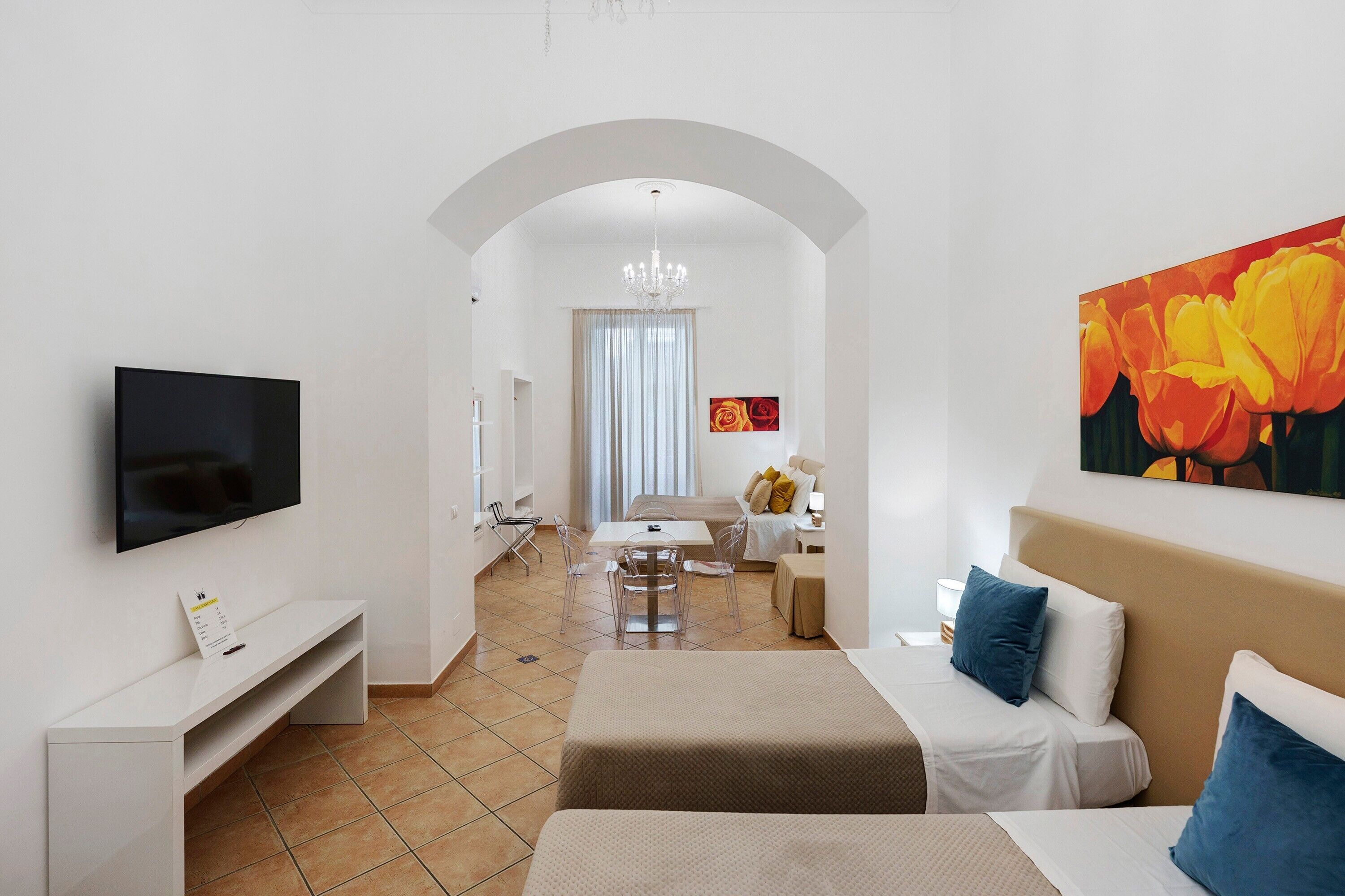 A modern living room with a flat-screen TV, a sofa, a dining table with chairs, and a hallway leading to a bedroom.