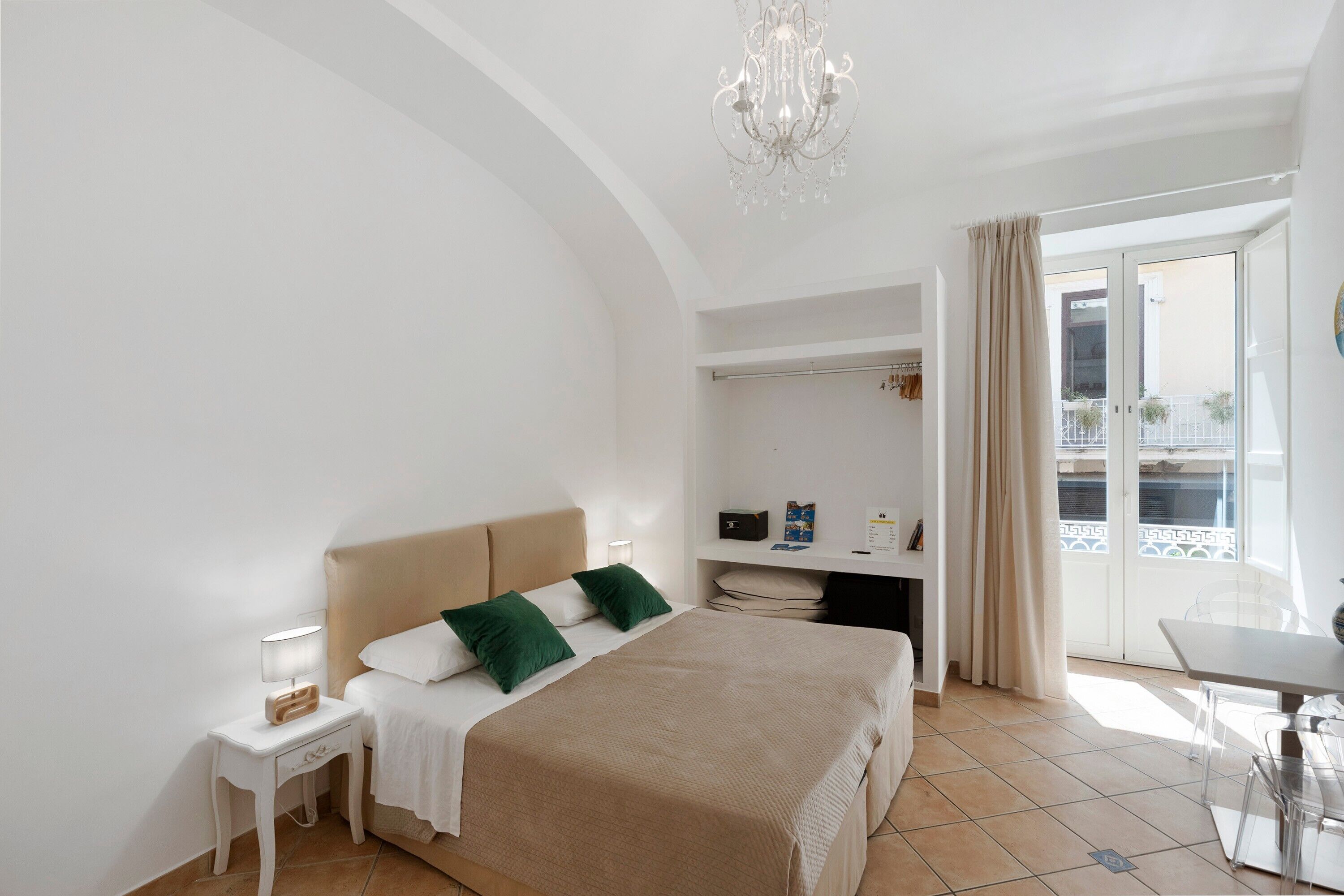Een hotelkamer met een groot bed, een bureau, een stoel, een kroonluchter en een balkon met uitzicht.
