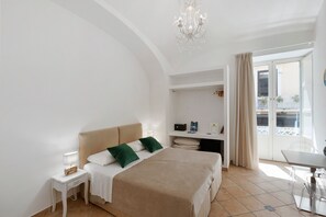 A hotel room with a large bed, a desk, a chair, a chandelier, and a balcony with a view.