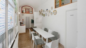 A dining area with a long table and chairs, a kitchen in the background, and decorative plates on the wall. - Sorrentina Guest House – Quadruple Room with Balcony and Wi-Fi (Sorrento)