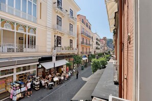 A street with cafes and shops, buildings with balconies, and a clear sky.