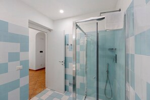 A bathroom with a glass-enclosed shower, tiled walls, and a wooden floor.