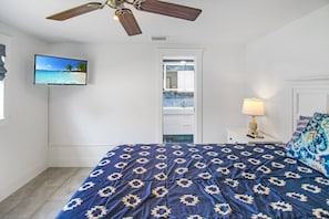 A bedroom with a bed, a ceiling fan, a TV, a nightstand, and a bathroom door. - Waterfront Paradise in Punta Gorda The Boat House (Punta Gorda)