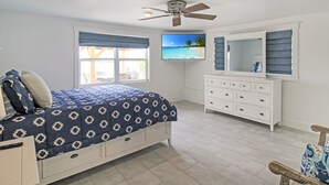 Une chambre à coucher comprenant un lit, une commode, un ventilateur de plafond, un téléviseur et une fenêtre donnant sur un paysage agréable.