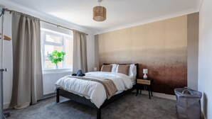 A bedroom with a bed, a nightstand, a lamp, a window with curtains, a plant, and a bag. - Perfect Booking 4 Bed Home With Parking for 2 (Bristol)