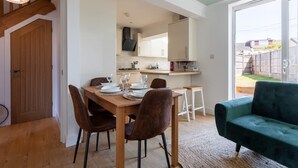 A dining area with a wooden table set for four, a green sofa, and a kitchen in the background. - Perfect Booking 4 Bed Home With Parking for 2 (Bristol)
