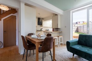 Ein Essbereich mit einem Holztisch, gedeckt für vier Personen, einer grünen Couch und einer Küche im Hintergrund.