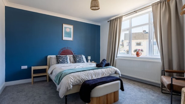 A bedroom with a bed, bedside tables, a window with curtains, a hanging light fixture, and a wall-mounted picture. - Perfect Booking 4 Bed Home With Parking for 2 (Bristol)