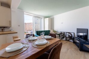 Ein Essbereich mit einem Holztisch, gedeckt für vier Personen, einem grünen Sofa und einem Fernseher im Hintergrund.