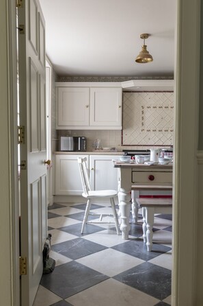 A kitchen with white cabinets, a microwave, a sink, and a dining area with a chair and table.