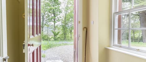 A hallway with a wooden door leading outside, a window with a view of trees, and a light fixture above.