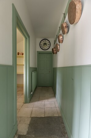 A hallway with a green door, a clock, and copper pots on the wall.