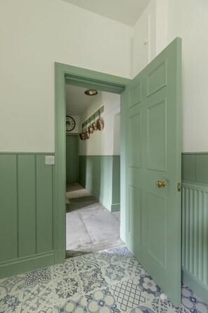 Un pasillo con una puerta verde, un interruptor de luz y un reloj en la pared.