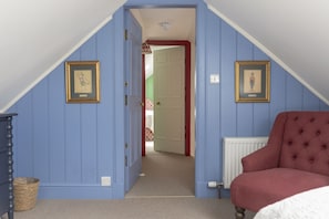 A room with a sloped ceiling, a red chair, a framed picture, and a radiator.