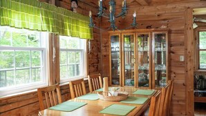 Comedor de madera con una gran mesa, sillas, candelabro y aparador con puertas de vidrio.
