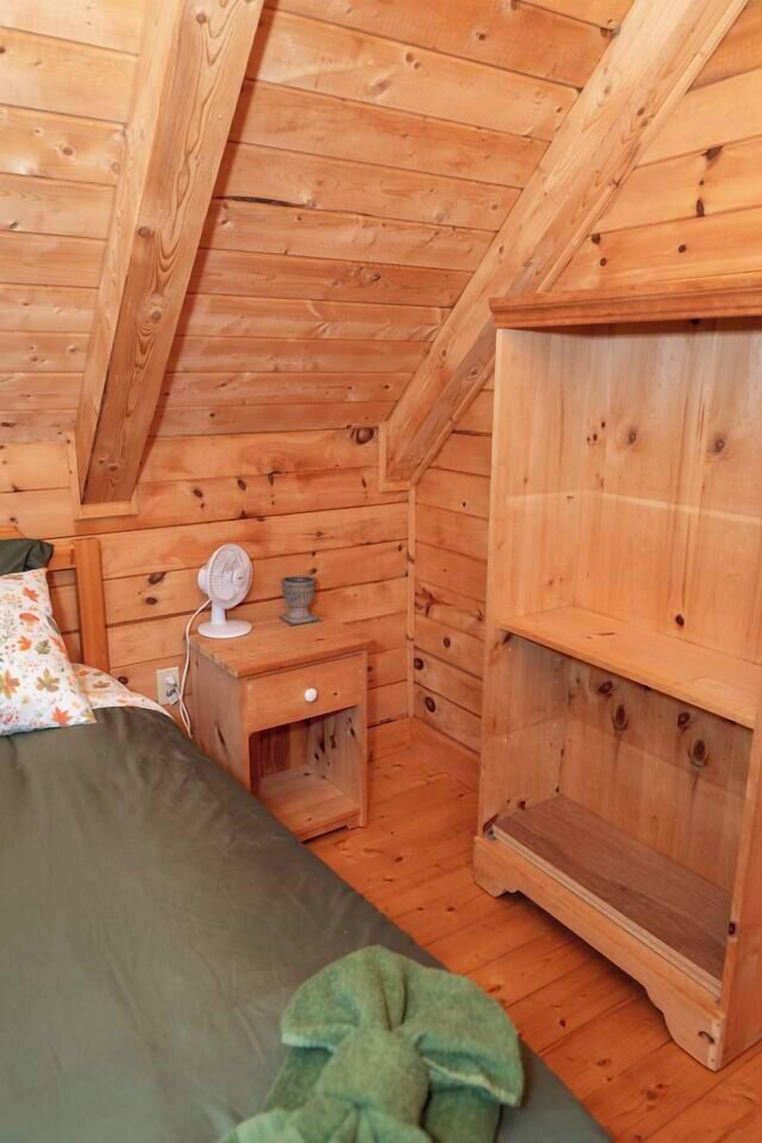 Une pièce de style cabane en bois, comprenant un lit, une table de chevet et une étagère.