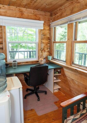 Interior de una cabaña con un escritorio de madera, una silla y ventanas con vistas a una terraza.