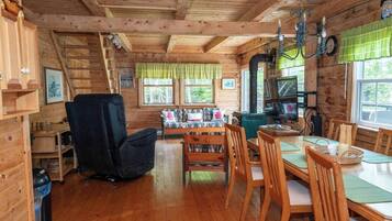 A cozy cabin interior with a dining area, wooden walls, and a fireplace.