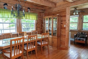 Interior d'una cabana de fusta amb una taula de dinar, cadires, un armari i una finestra.