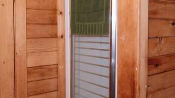 A wooden interior with a glass door leading to a shower area, a towel hanging on the door, and a toilet paper holder on the wall.