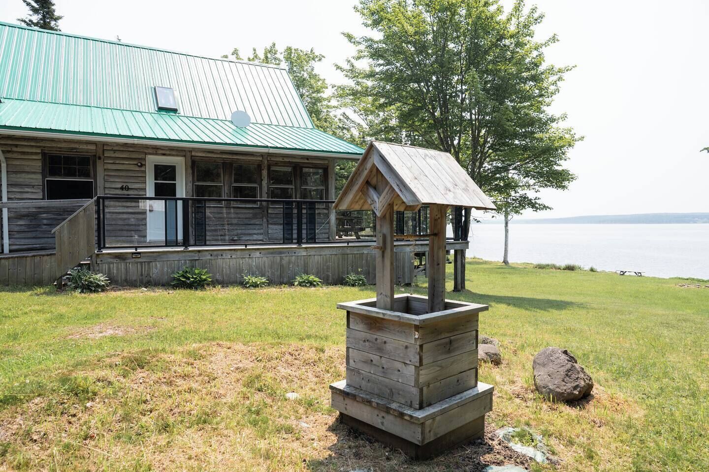A rustic wooden building with a green roof, a wooden birdhouse, and a grassy area with a view of the water.