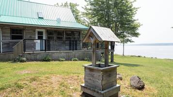 A rustic wooden building with a green roof, a wooden birdhouse, and a grassy area with a view of the water.